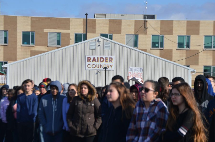 A student in the crowd holds up a sign that reads "We Need Change."