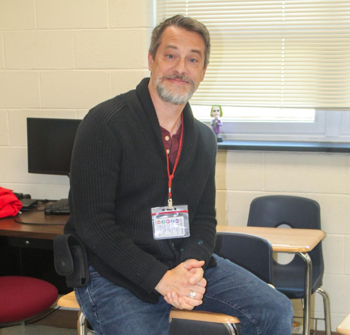 Mr. Eberle sits on top of a desk in his classroom