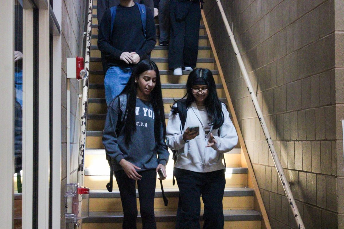 Phones in hands, students walk down the stairs during passing time. Under the current policy students are permitted to use their phones between classes.