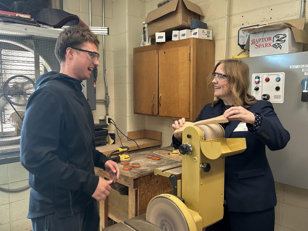 Senior student Spencer Marso assists Commissioner of Education Lily Laux in making her own wooden scraper inside room 502.